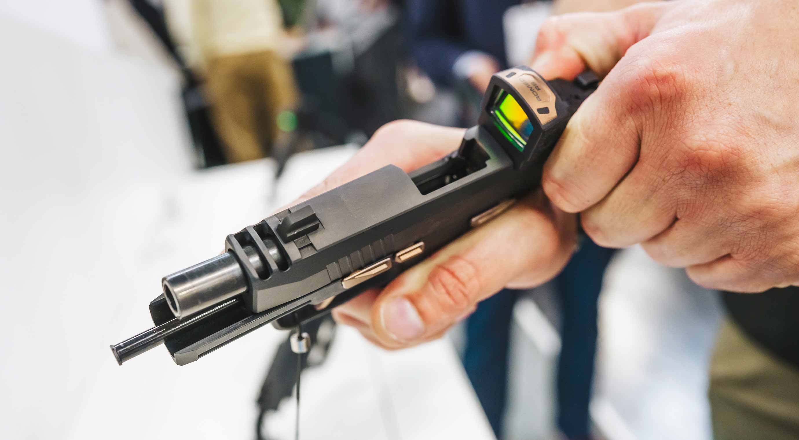 Close-up of a semi-automatic pistol with a red-dot sight mounted on it, held in someone's hands at a exhibition stand.