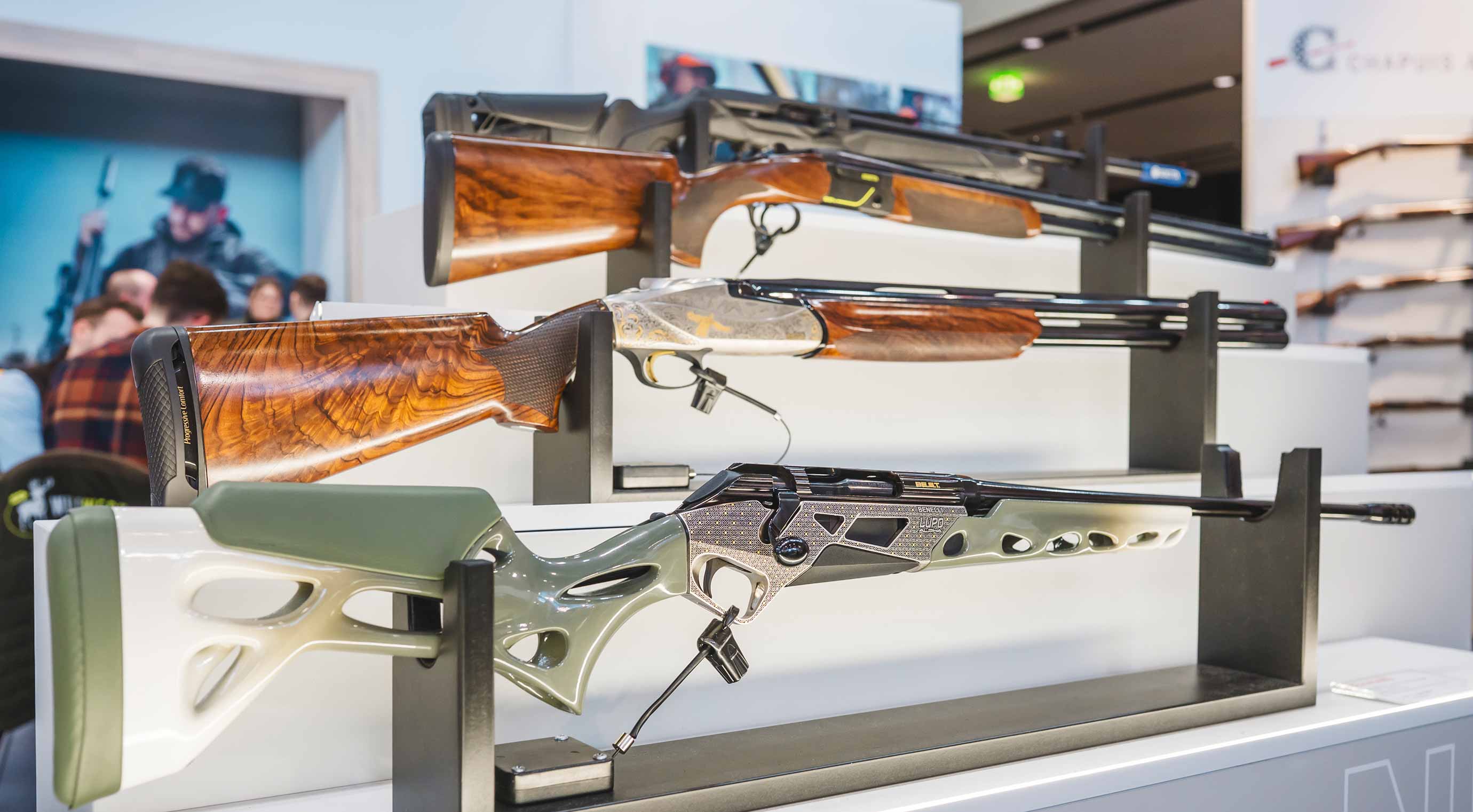 Several firearms with wooden and plastic stocks on display in a holder at a exhibition stand.