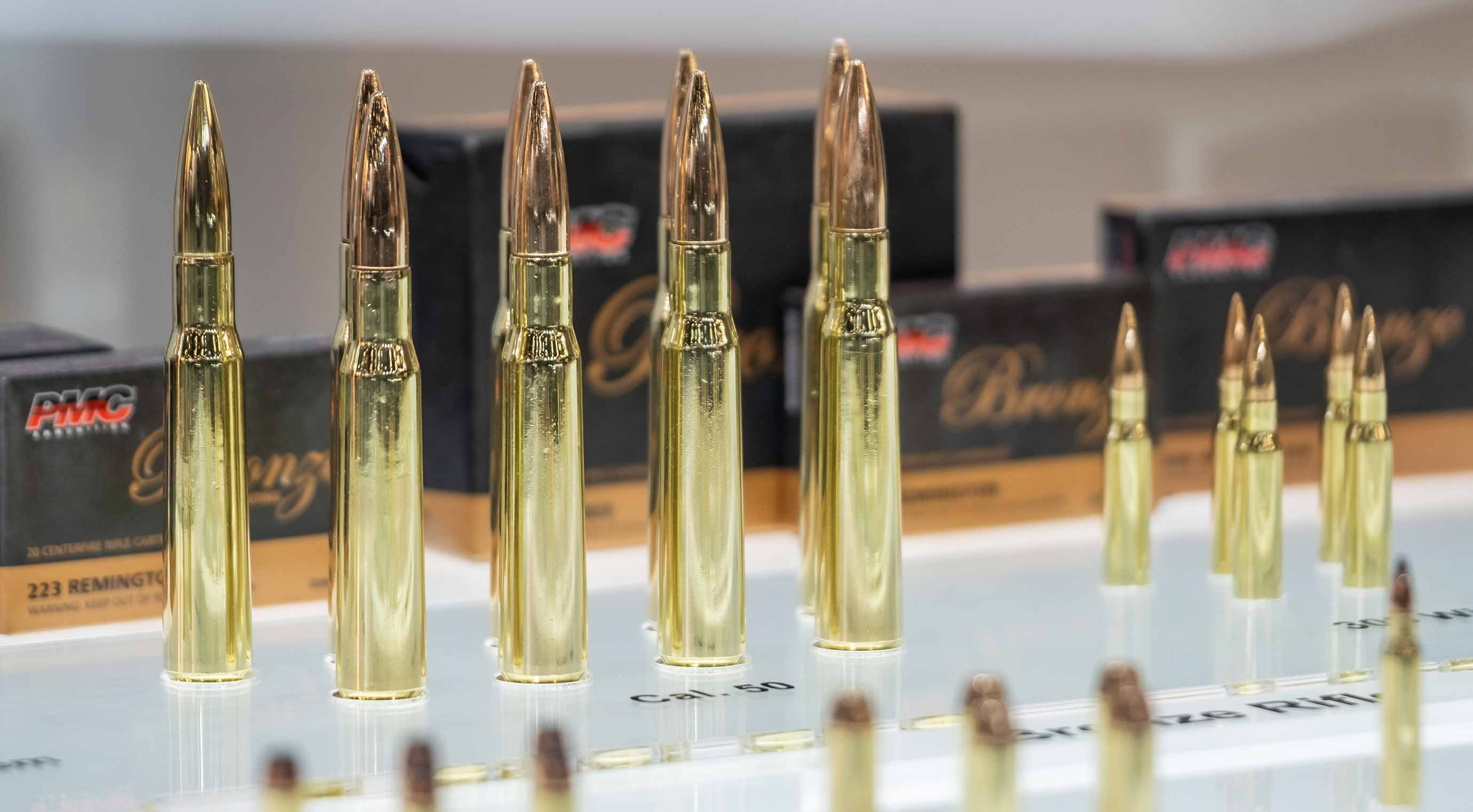Rifle ammunition of various calibers lined up in front of packaging at a exhibition stand.