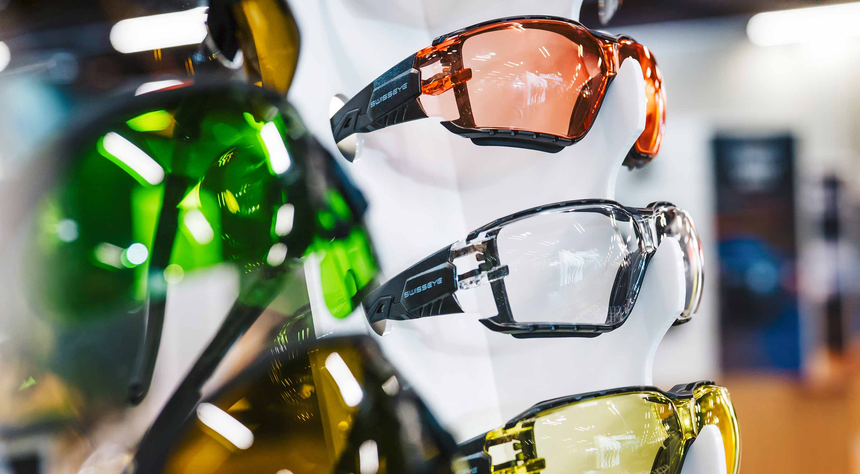 Safety glasses with colored lenses on display as part of a product presentation at an exhibition stand.