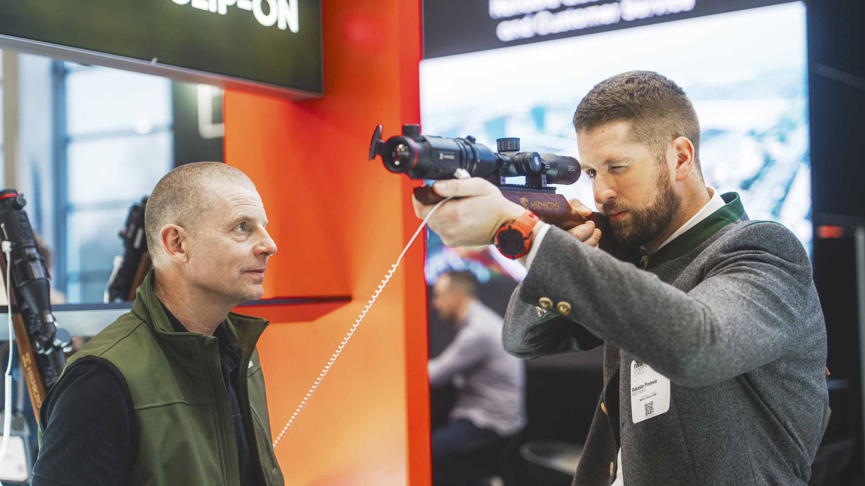 Two men at a trade fair stand, one of them looking through a telescope