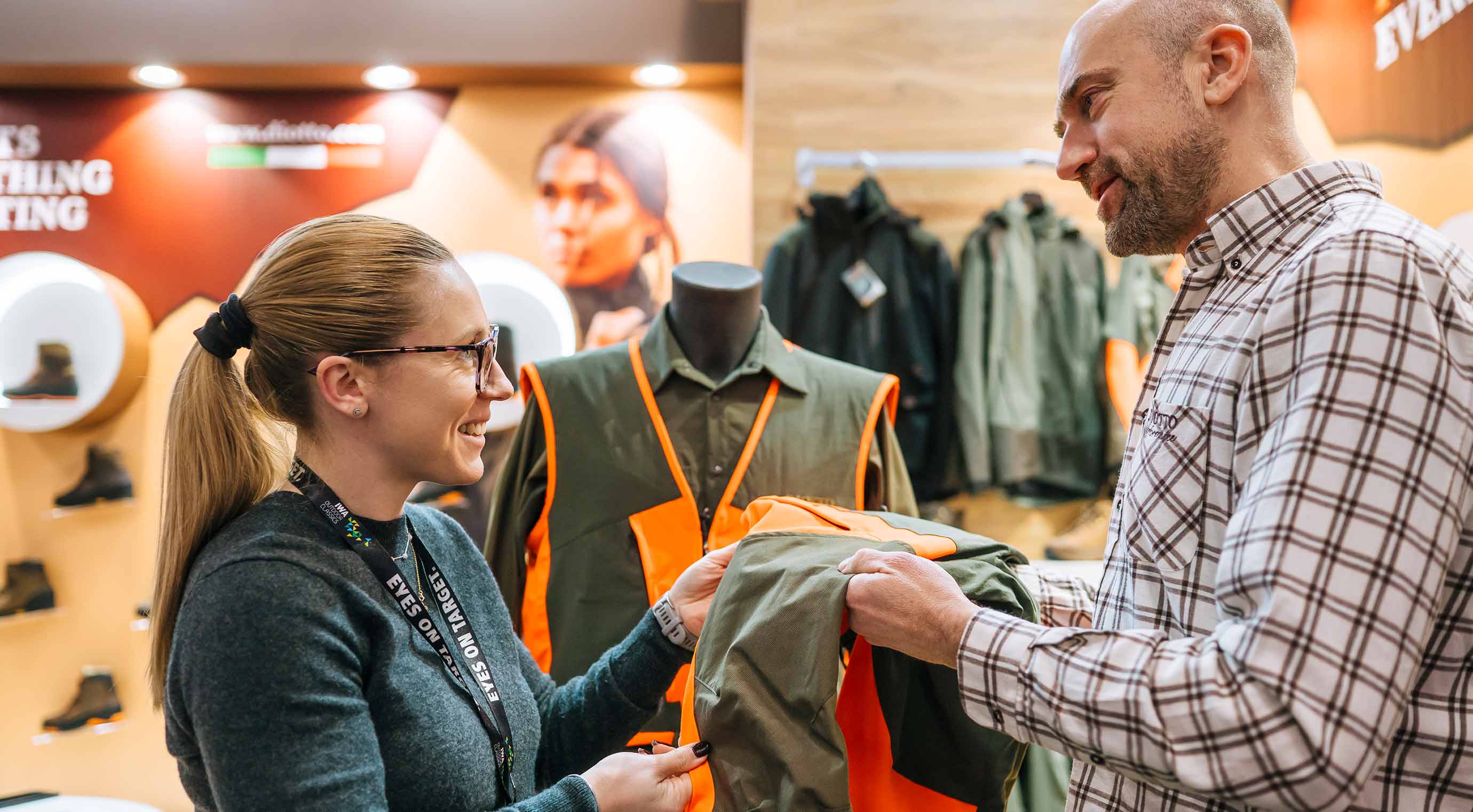 A visitor checks out hunting clothing in high-visibility colors at a exhibition stand for outdoor and hunting gear.